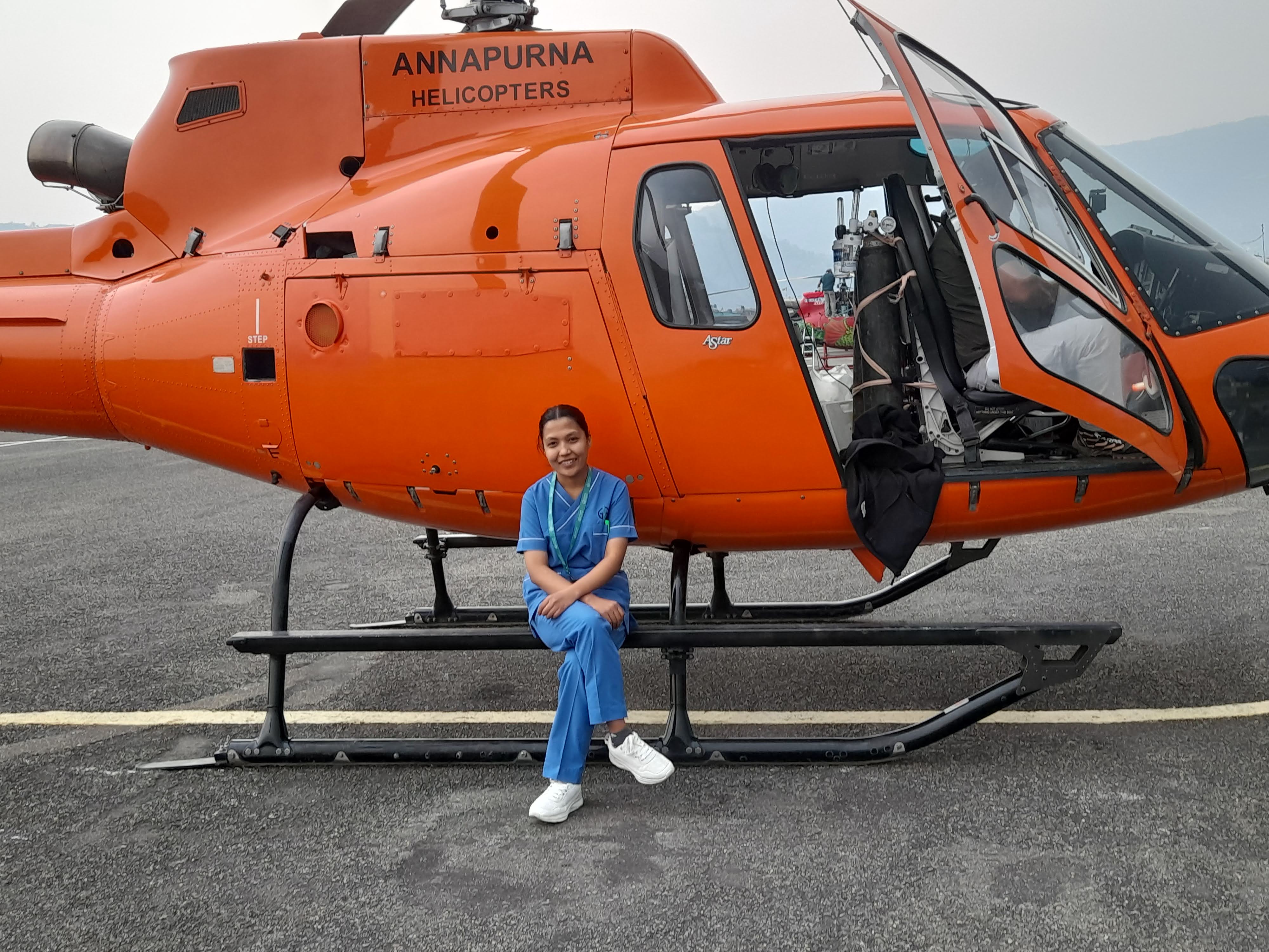 Deepa Shrestha in scrubs beside an Annapurna Helicopters air ambulance